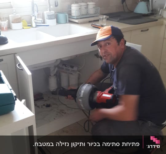 אינסטלטור עובד מתחת לכיור עם כלי עבודה חשמלי